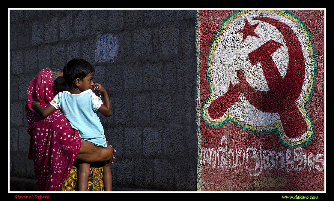 Mother and son by Hammer and Sickle wall painting, Kerala, India